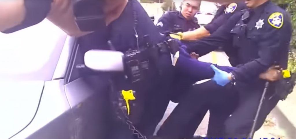 A still from the video shows Oakland police officers trying to pull Demouria Hogg from the car after he's been shot.