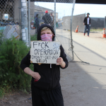 Jessica Bailey, who is unhoused, poses at Wood St, where she currently lives, with a sign she brought to the protest outside of Mayor Libby Schaaf's home on Monday. Her sign criticizes Operation Dignity, the non-profit who has contracted with the city of Oakland to run the Tuff Shed site that Baily lived in for over three months. Photo by Zack Haber.